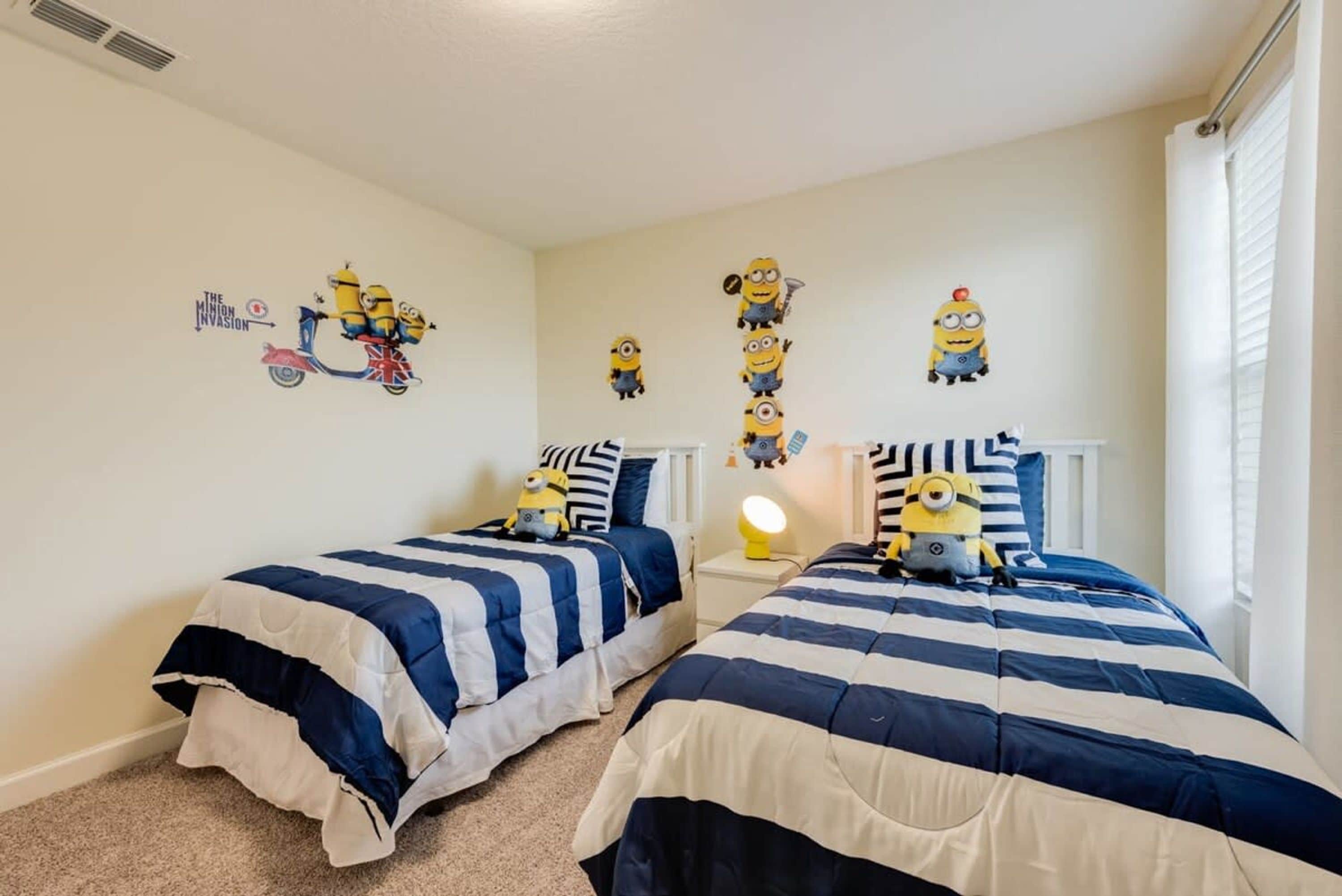 Un dormitorio con dos camas, cada una con una colcha azul y blanca a rayas, y una pared decorada con pegatinas de minions.