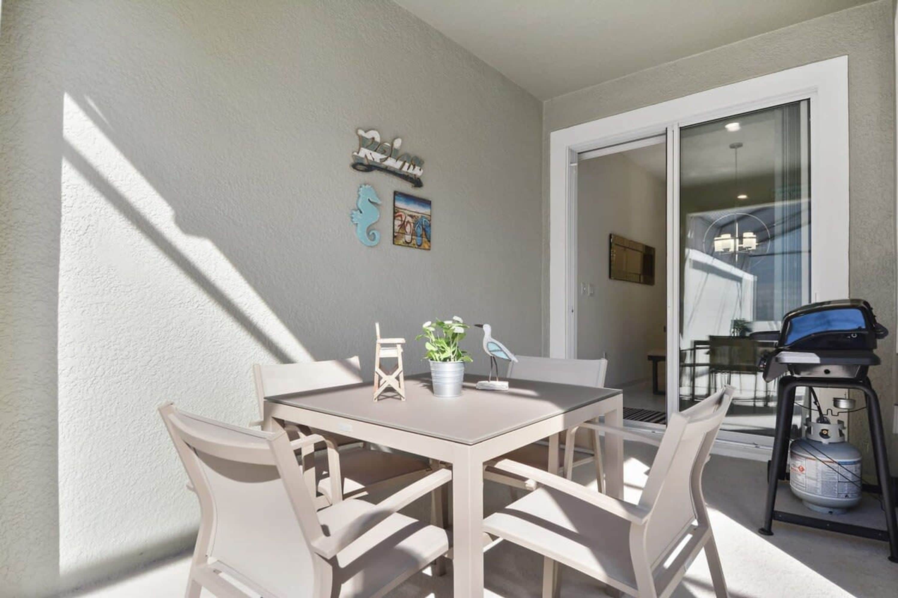 A dining area with a table and chairs, a potted plant, and a grill outside.