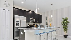 A modern kitchen with dark cabinets, stainless steel appliances, a central island with bar stools, and a potted plant.