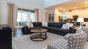 A modern living room with a sectional sofa, a round coffee table, and patterned ottoman. - Spacious Comfy Retreat Prime Location Amazing (Kissimmee)
