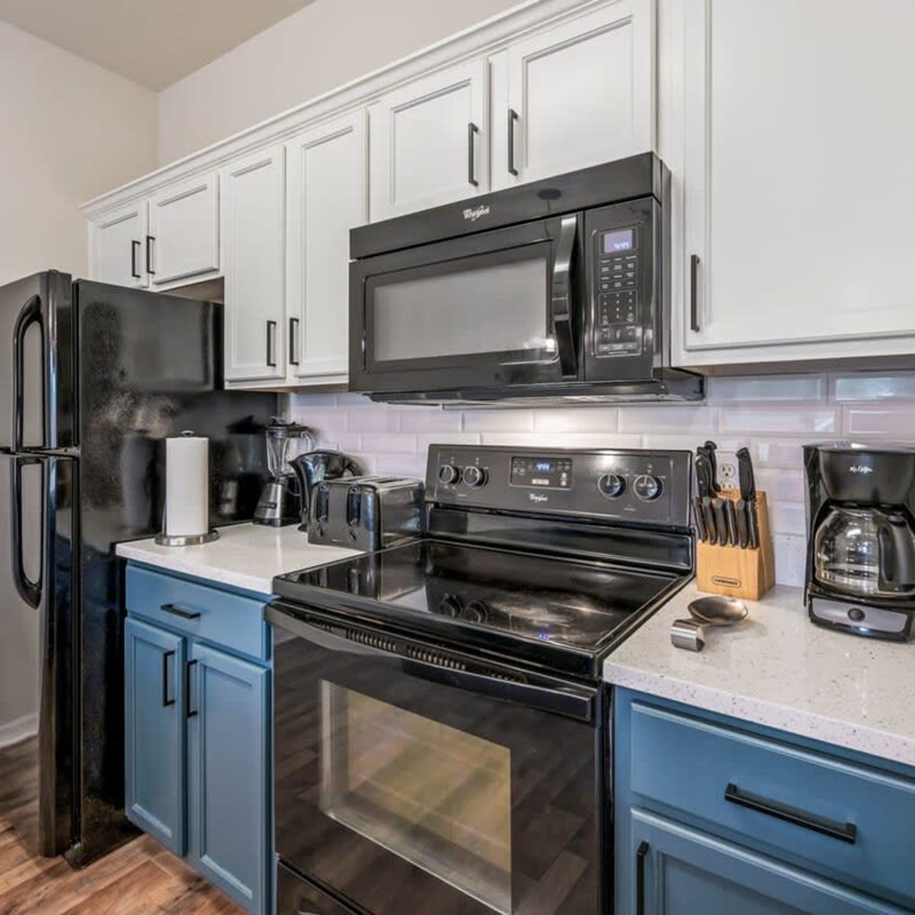 A modern kitchen with white cabinets, a black microwave, a stainless steel refrigerator, a gas stove, and a coffee maker.