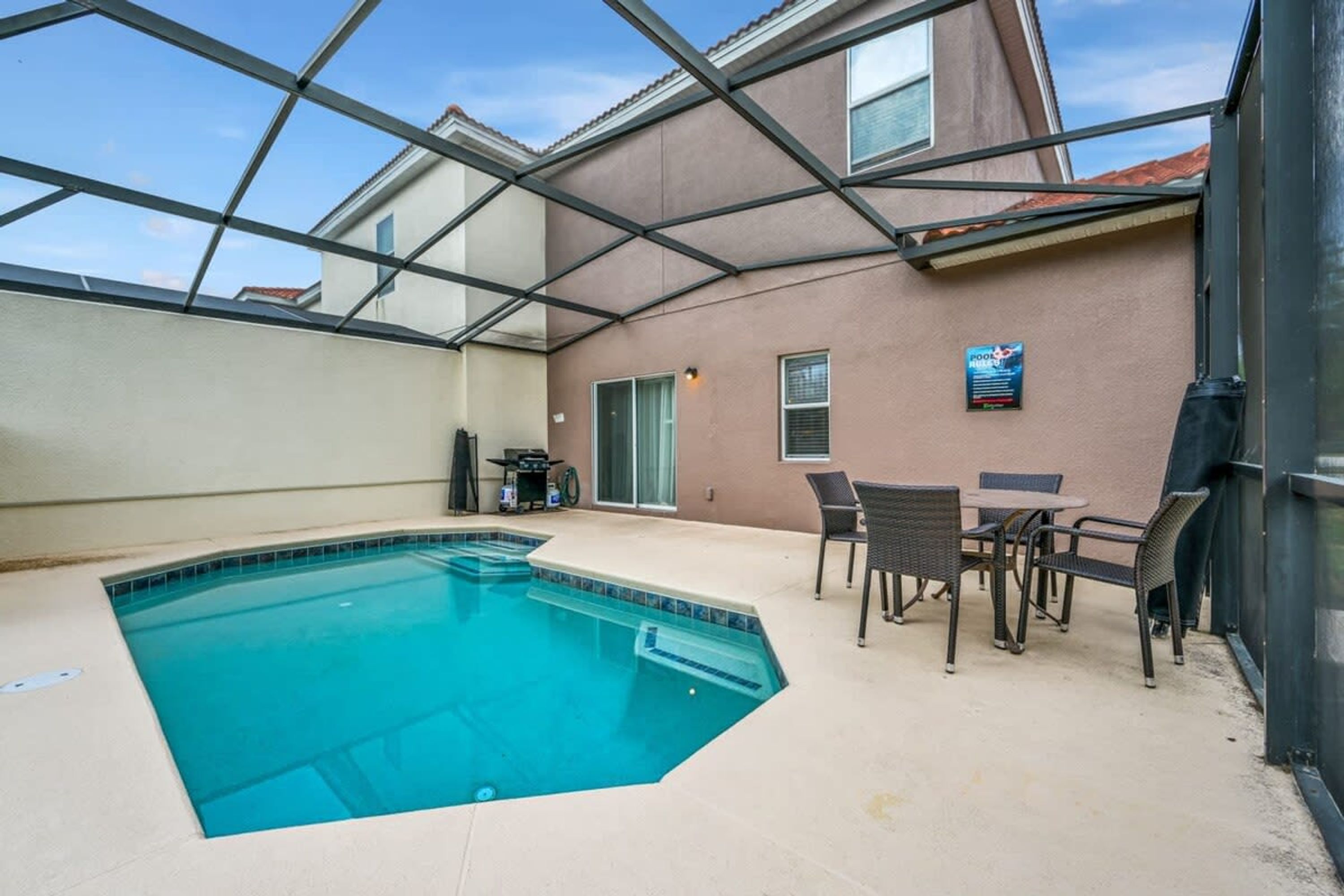 Ein Schwimmbecken mit Glasdach, eine Terrasse mit Sitzgelegenheiten und ein Schild, das den Poolbereich kennzeichnet.