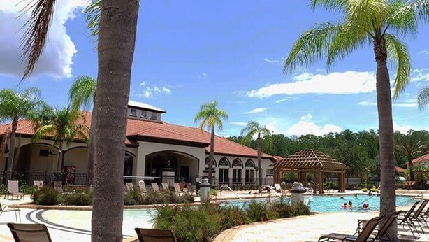 Een resort met een zwembad, ligbedden, palmbomen en een gebouw met een rood dak.