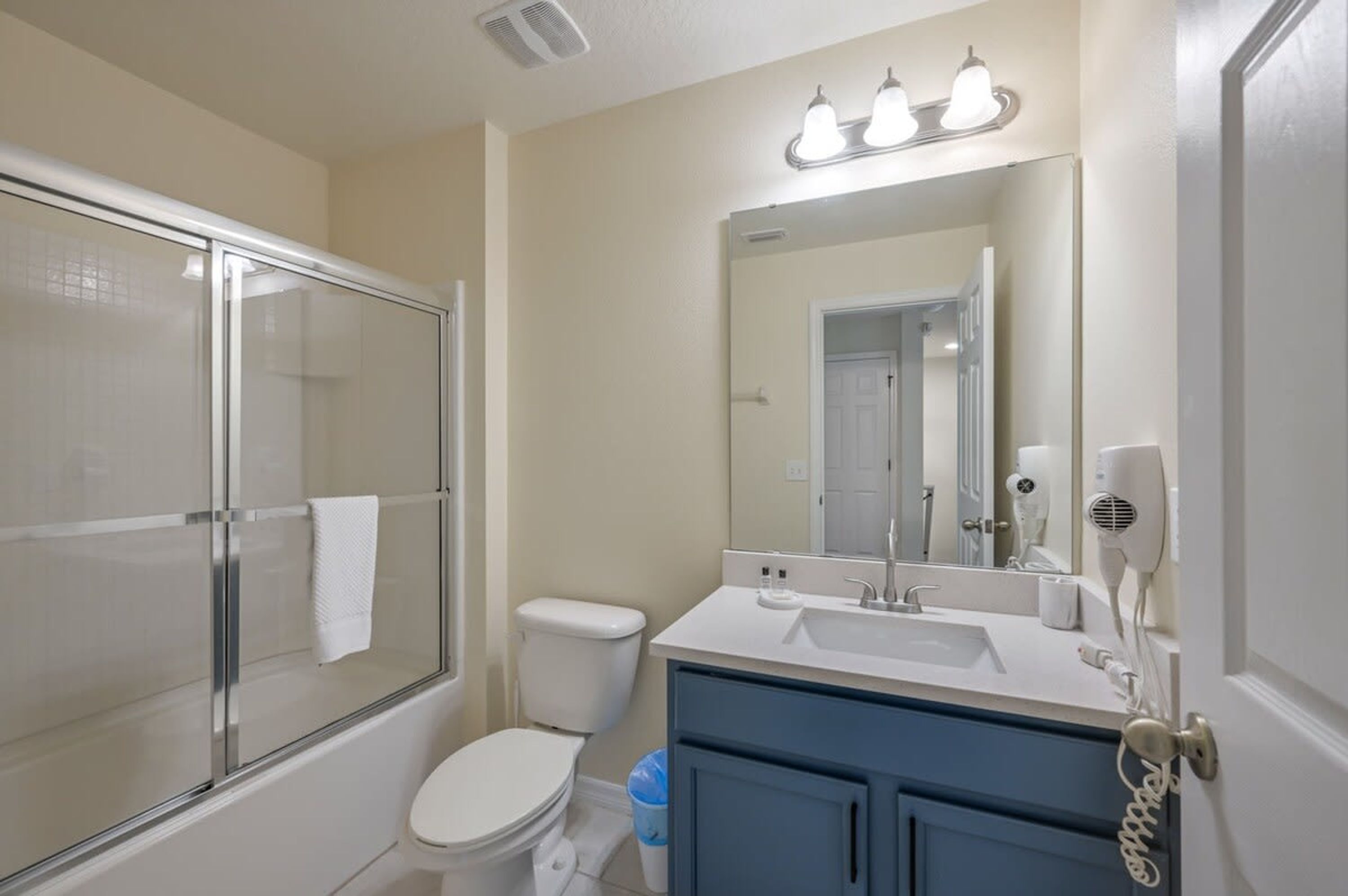 A bathroom with a glass shower enclosure, a white toilet, a sink with a mirror, and a hairdryer on the wall.
