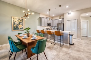 A modern kitchen with grey cabinets, a stainless steel refrigerator, and a central island with bar stools. - Spacious Condo-modern Decor Star Wars Bedroom (Davenport)