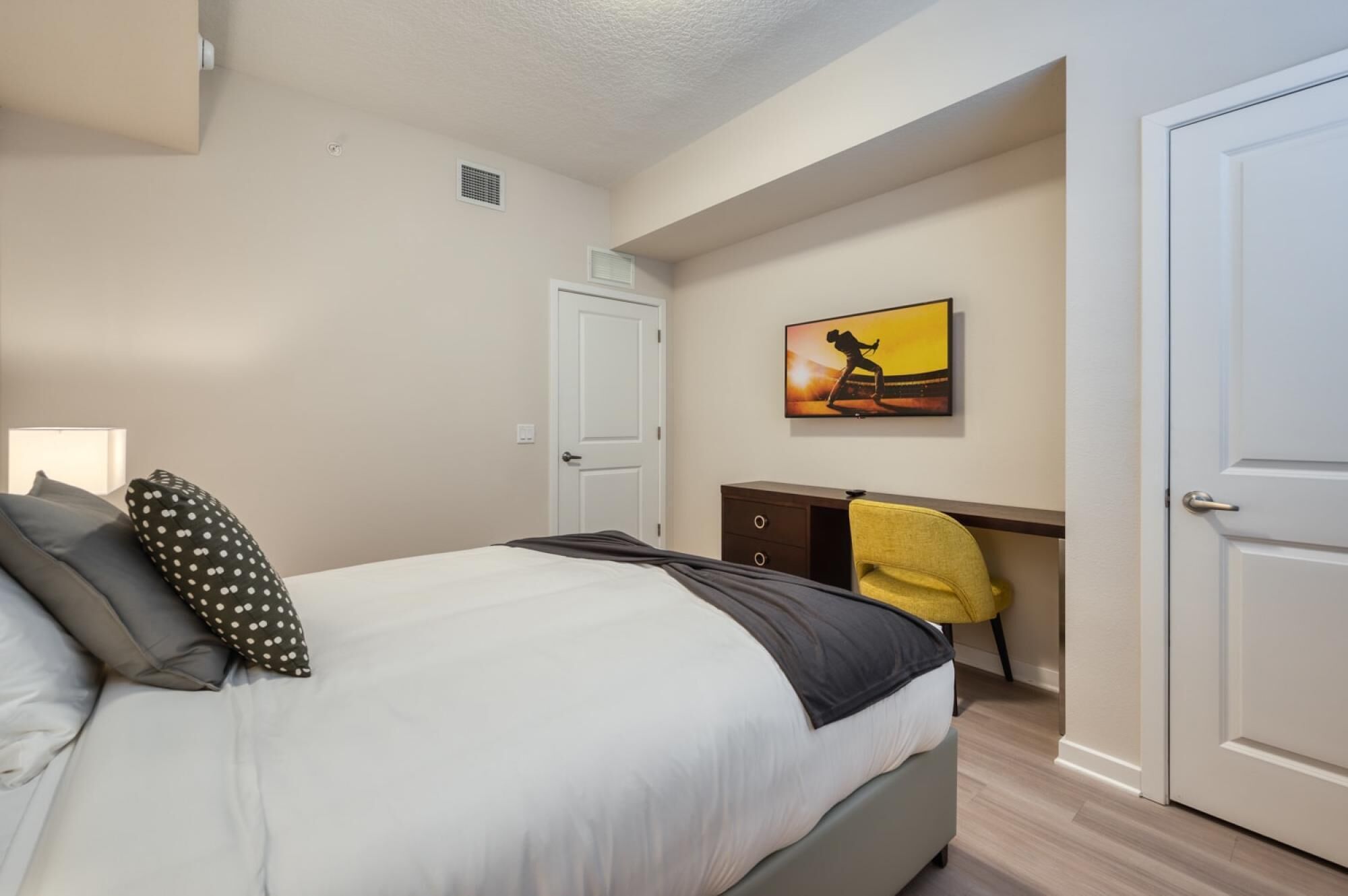 A bedroom with a bed, a desk, a chair, and a painting on the wall.