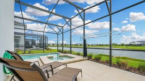 A covered patio with a pool, lounge chairs, and a view of a lake and greenery. - Luxury Storey Lake Retreat - Spacious Disney-near (Kissimmee)
