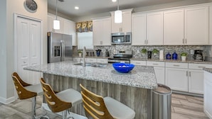 A modern kitchen with white cabinets, granite countertops, stainless steel appliances, and a blue bowl on the island. - Luxury Storey Lake Retreat - Spacious Disney-near (Kissimmee)