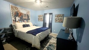 Ein Schlafzimmer mit einem Bett, einem Schreibtisch, einer Lampe und Bildern an den Wänden.