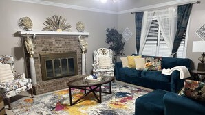 Ein Wohnzimmer mit Kamin aus Backstein, einem blauen Sofa, einem gemusterten Sessel und einem Couchtisch.