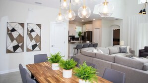 A modern living room with a wooden dining table, grey sofas, and hanging spherical pendant lights. - Stunning 5BR Home - Your Dream Getaway (Kissimmee)