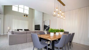 A modern living room with a sofa, dining table, chairs, and a TV. - Stunning 5BR Home - Your Dream Getaway (Kissimmee)
