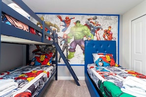 Une chambre avec des lits superposés, un mur décoré d’une fresque sur le thème des super-héros et une fenêtre donnant sur le ciel.