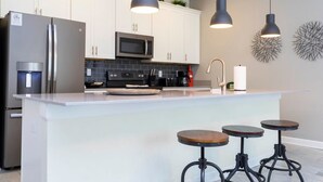 A modern kitchen with white cabinets, stainless steel appliances, a central island with stools, pendant lighting, and decorative wall art. - Themed Bedrooms Private Pool Amazing Location - Super Cute Home (Davenport)