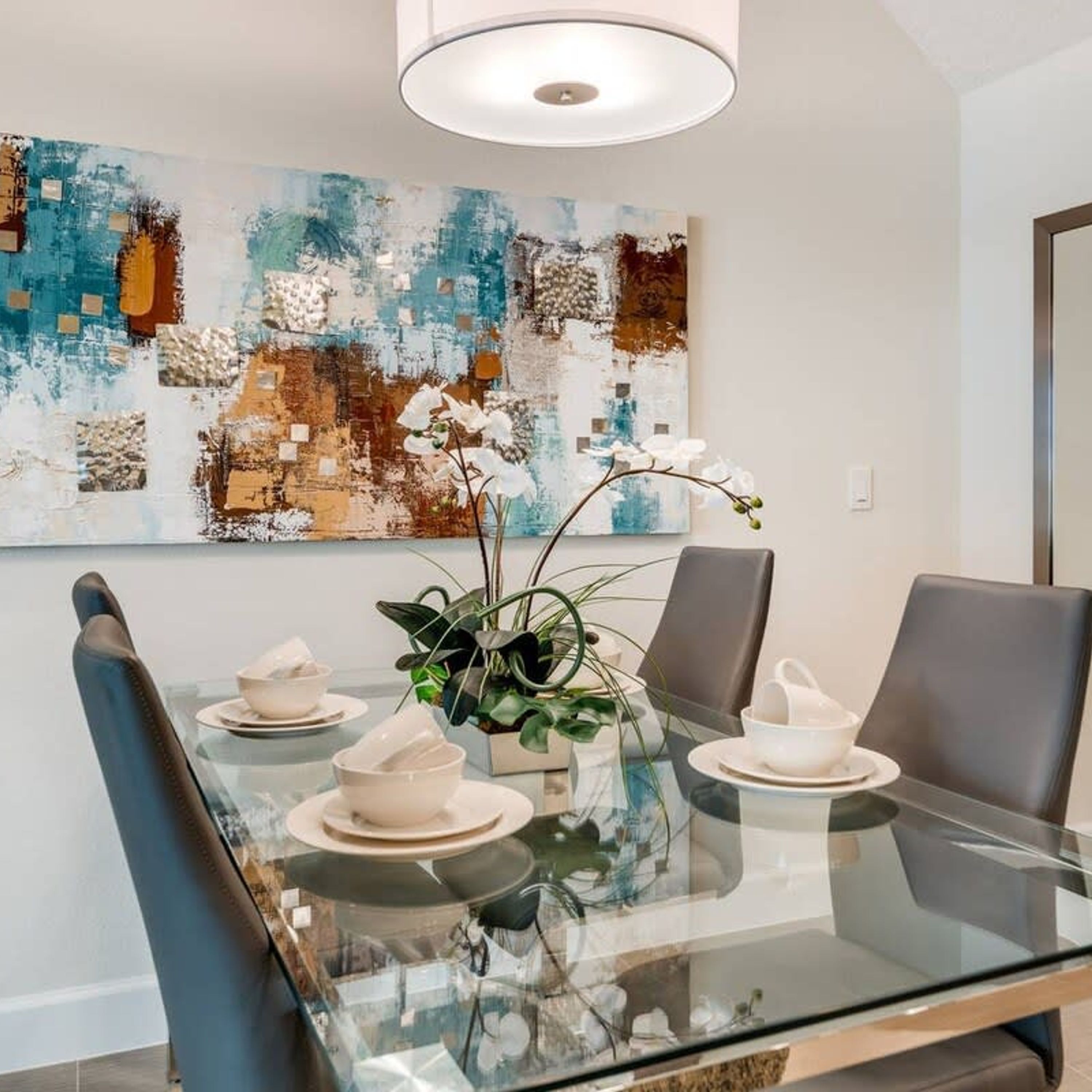 A modern dining area with a glass table, black chairs, and a decorative orchid centerpiece.