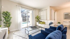 A modern living room with a glass coffee table, a blue sofa, a white sofa, and a large window with curtains. - Themed 4BR Home-mickey Star Wars Pool Spacious (Kissimmee)