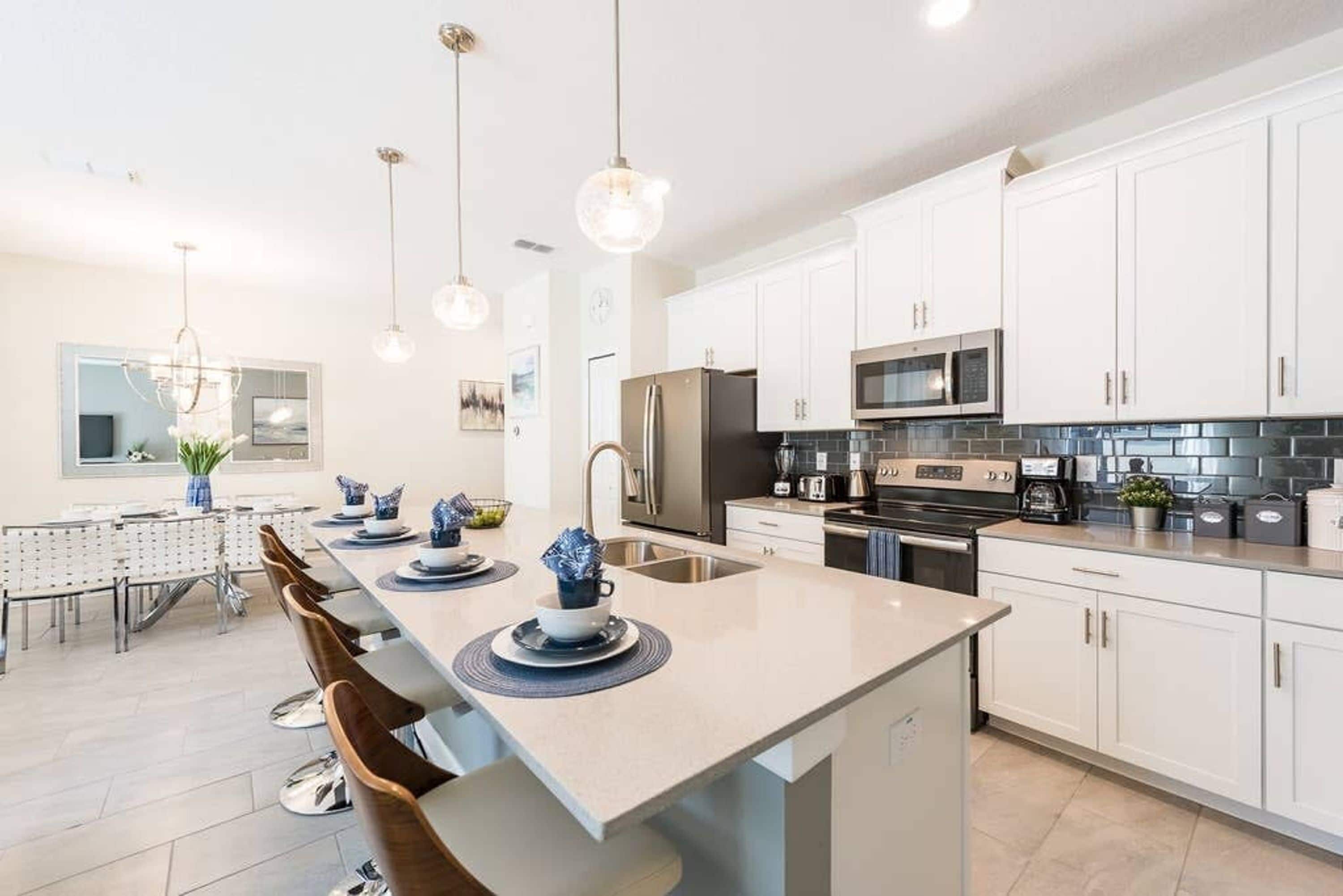 A modern kitchen with white cabinets, stainless steel appliances, and pendant lighting.