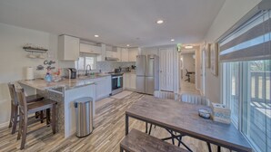 Een moderne keuken met een centraal eiland, witte kasten, roestvrijstalen apparatuur en een eethoek met een houten tafel en stoelen.