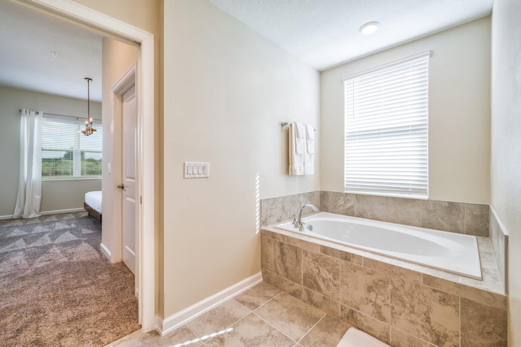 A bathroom with a large bathtub, a shower, and a toilet. There is a window with blinds and a towel hanging on the wall.