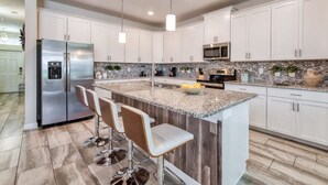 A modern kitchen with white cabinets, stainless steel appliances, a granite countertop, and bar stools. - Stunning Home Private Pool Great Location (Kissimmee)