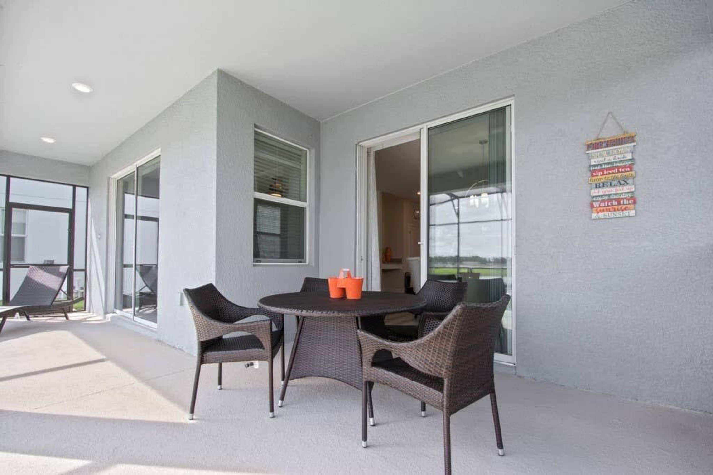 Un patio techado al aire libre con una mesa redonda y sillas de mimbre, ventanas amplias y un letrero en la pared.