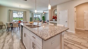 A modern kitchen with granite countertops, a dining area with chairs, and a view of the outdoors. - Stunning Home Private Pool Great Location (Kissimmee)