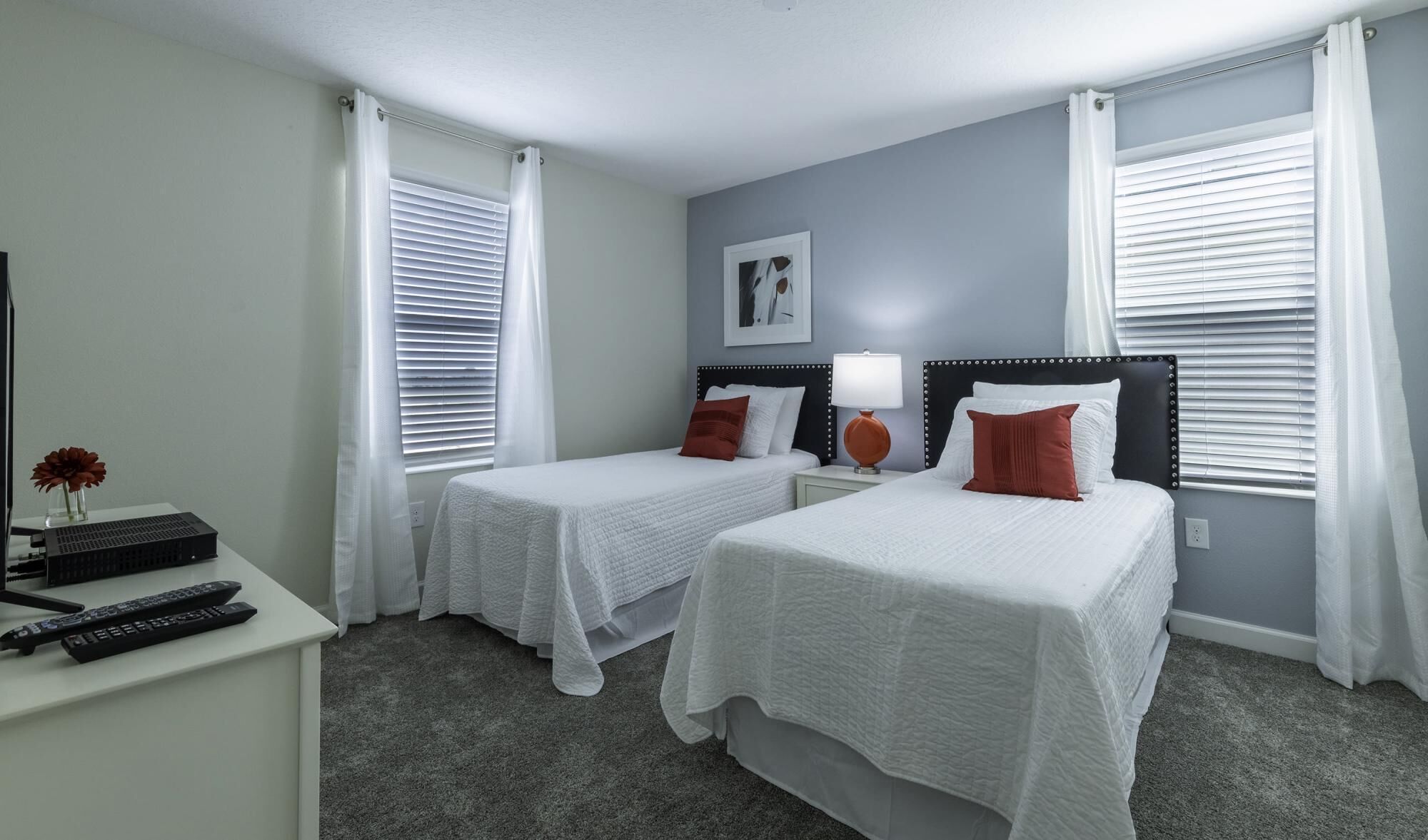 A hotel room with two single beds, a desk with a computer and keyboard, a lamp, and a framed picture on the wall.