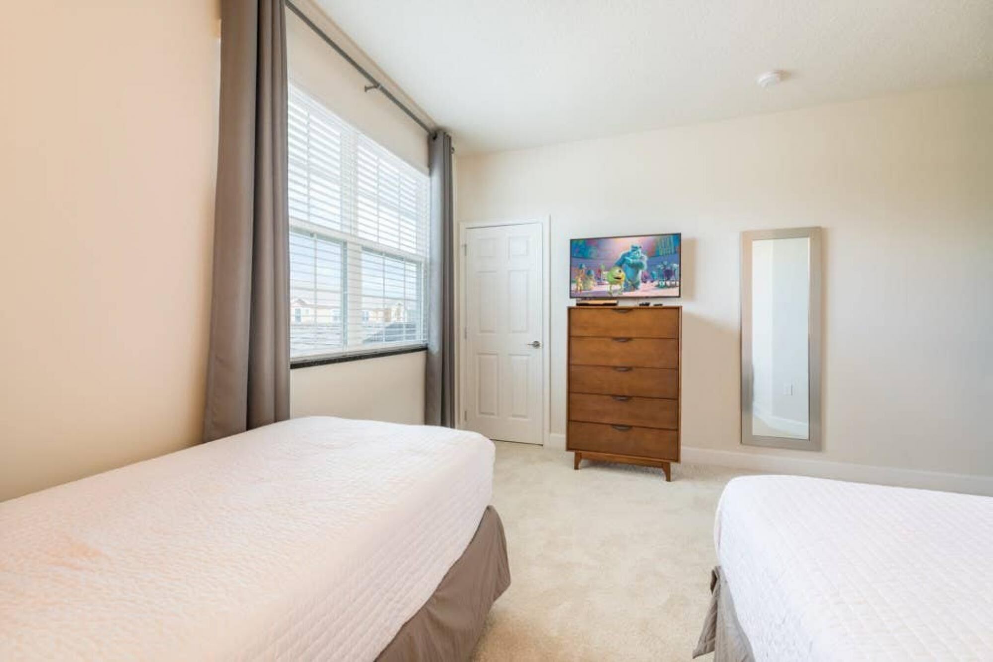 Une chambre avec deux lits, une commode, un téléviseur et une fenêtre avec des stores.