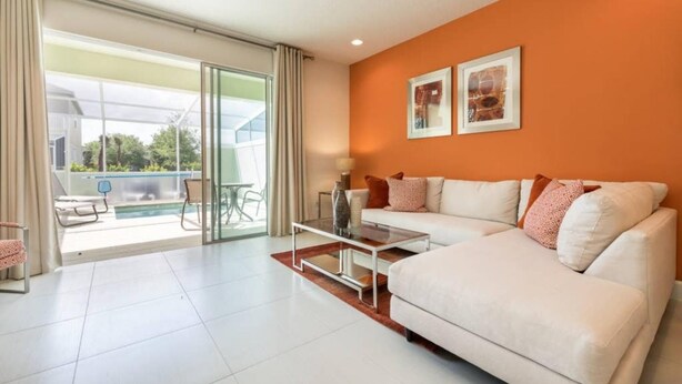 Un salón moderno con un sofá blanco, una mesa de centro de cristal y vistas a un área de piscina exterior a través de grandes puertas correderas de vidrio.