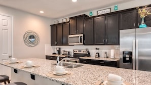 A modern kitchen with dark cabinets, stainless steel appliances, a granite countertop, and bar stools. - Ultimate Resort Retreat Stunning 6-bedroom Haven (Kissimmee)