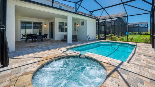 A covered outdoor swimming pool with a hot tub, patio seating, and a view of the surrounding area. - Ultimate Resort Retreat Stunning 6-bedroom Haven (Kissimmee)