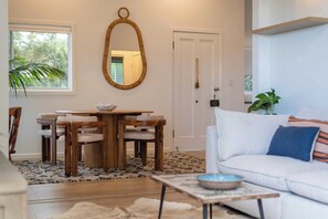 A modern living room with a wooden dining table, white sofa, and a large mirror. - Sunset Cottage - Pet Friendly- Oceanstays (Yamba)