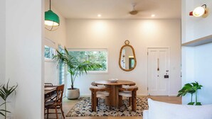 A dining area with a round wooden table, chairs, a potted plant, and a patterned rug. - Sunset Cottage - Pet Friendly- Oceanstays (Yamba)
