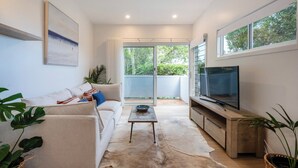 A modern living room with a sofa, coffee table, TV, and large windows. - Sunset Cottage - Pet Friendly- Oceanstays (Yamba)