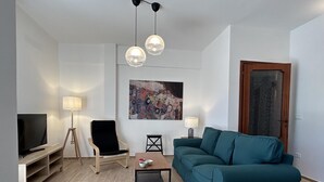 A modern living room with a teal sofa, a wooden TV stand, a black chair, and a coffee table. There is a painting on the wall and a door with a frosted glass panel. - Casa La Pigna in Pisa (Pisa)