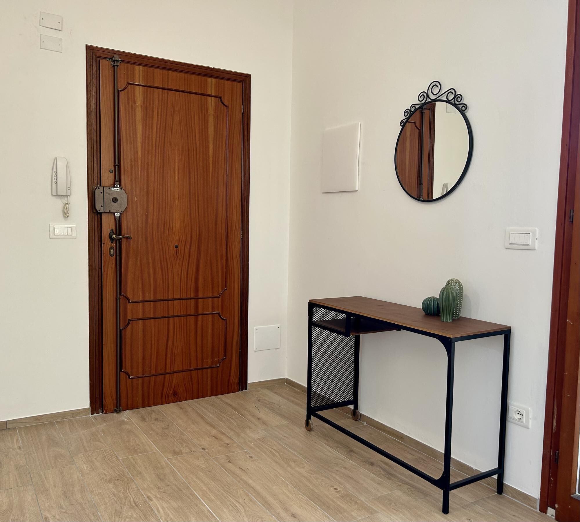 Une pièce avec une porte en bois, une petite table sur laquelle se trouve un cactus et un miroir rond accroché au mur.