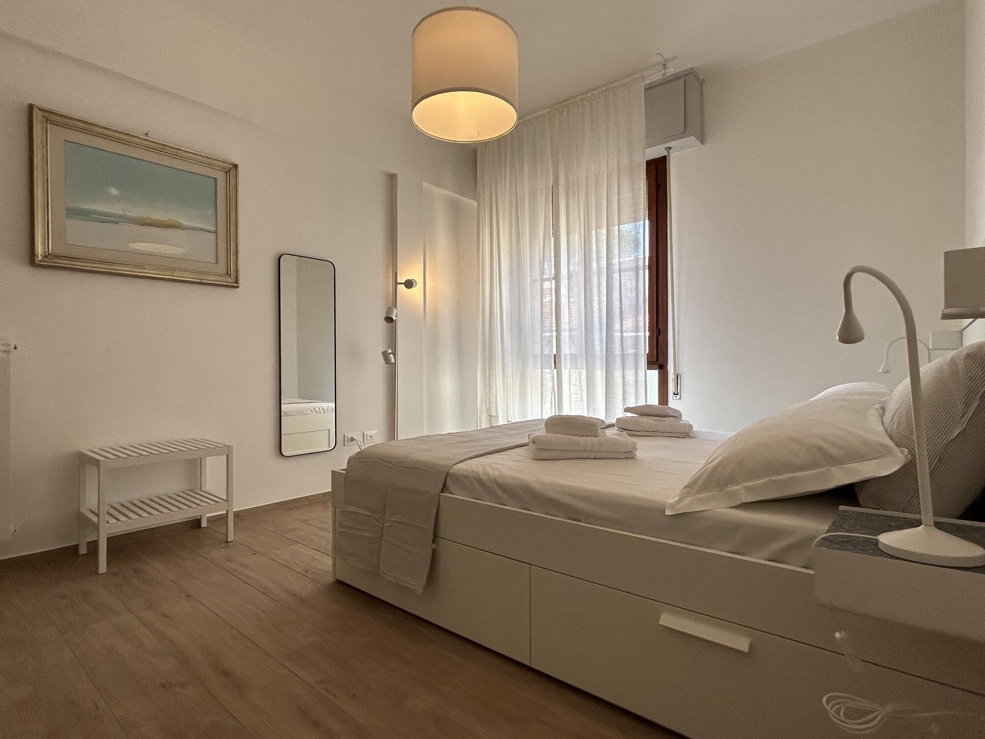 Un dormitorio moderno con cama, mesita de noche, lámpara y ventana con cortinas.