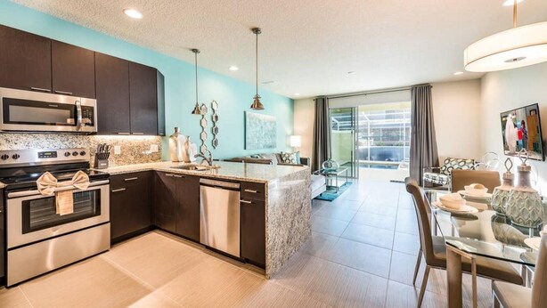 A modern kitchen with dark cabinets, stainless steel appliances, and a granite countertop. - Super Cozy Home With Private Pool (Clermont)