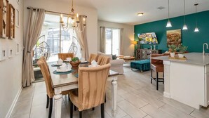 Une cuisine moderne avec un îlot central blanc, un coin repas avec des chaises beige et un mur d’accent de couleur turquoise.