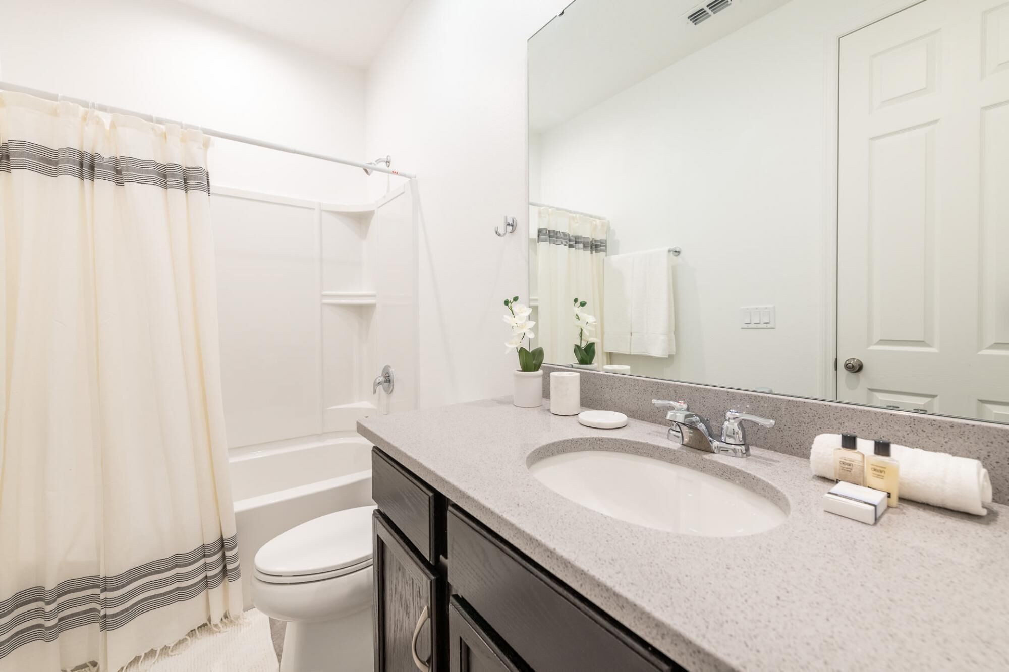 A bathroom with a shower, toilet, sink, and mirror.