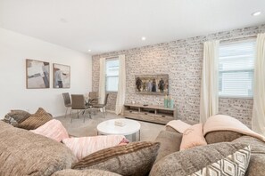 A modern living room with a brick wall, a flat-screen TV, a dining area, and a cozy seating arrangement.