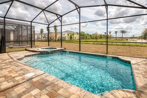 A swimming pool with a hot tub, surrounded by a glass enclosure, with a view of residential buildings and a grassy area.
