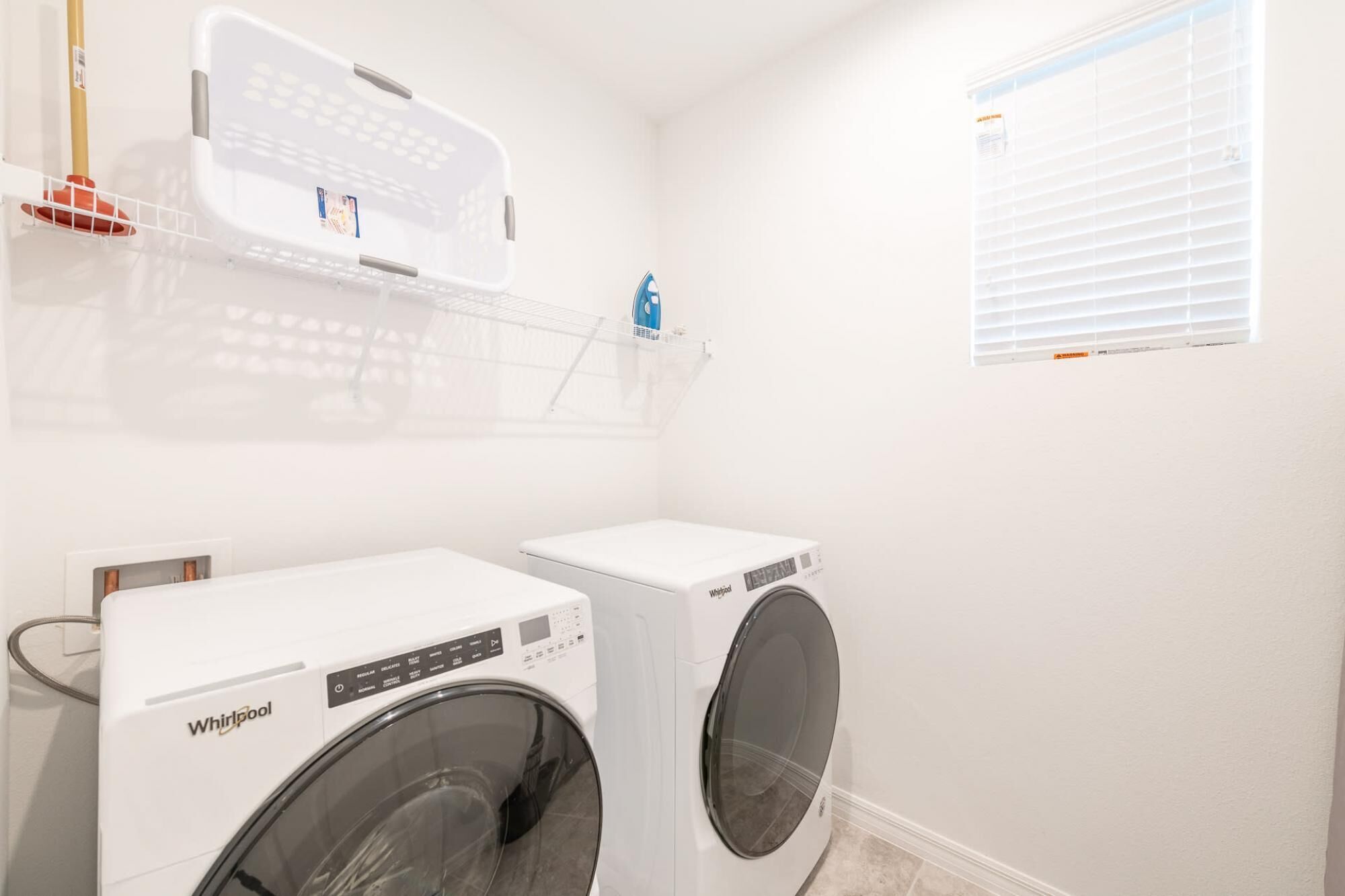 Une buanderie équipée de deux lave-linge Whirlpool, d’un étendoir et d’une fenêtre avec des stores.