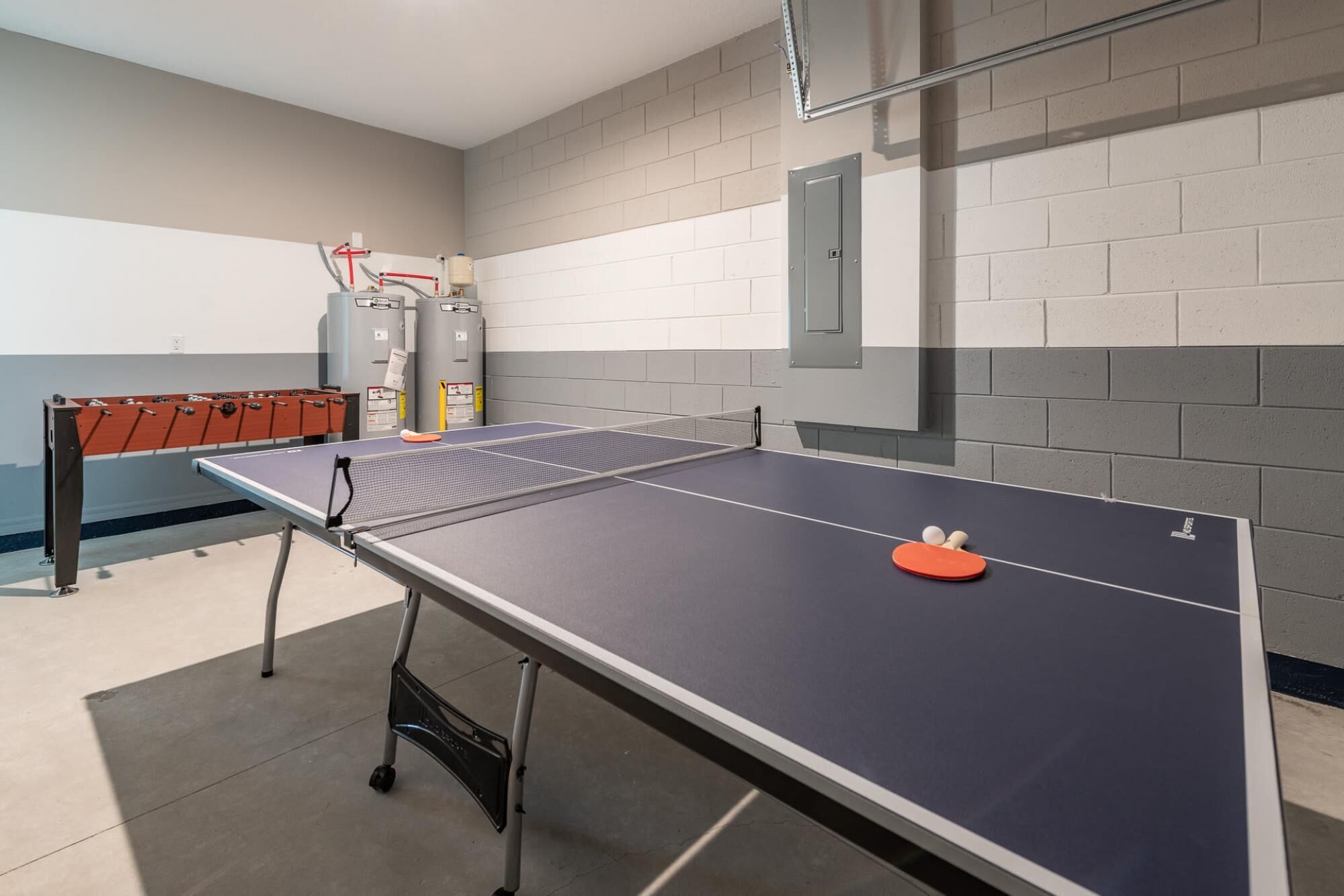 Une table de ping-pong avec un filet, dans une pièce dont un mur est en briques et qui contient également un chauffe-eau.