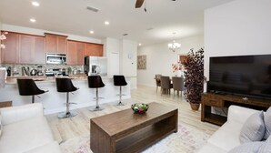 A modern living room with a TV, sofa, coffee table, and a dining area with chairs. - Private Pool Prime Location Beautiful Home (Kissimmee)