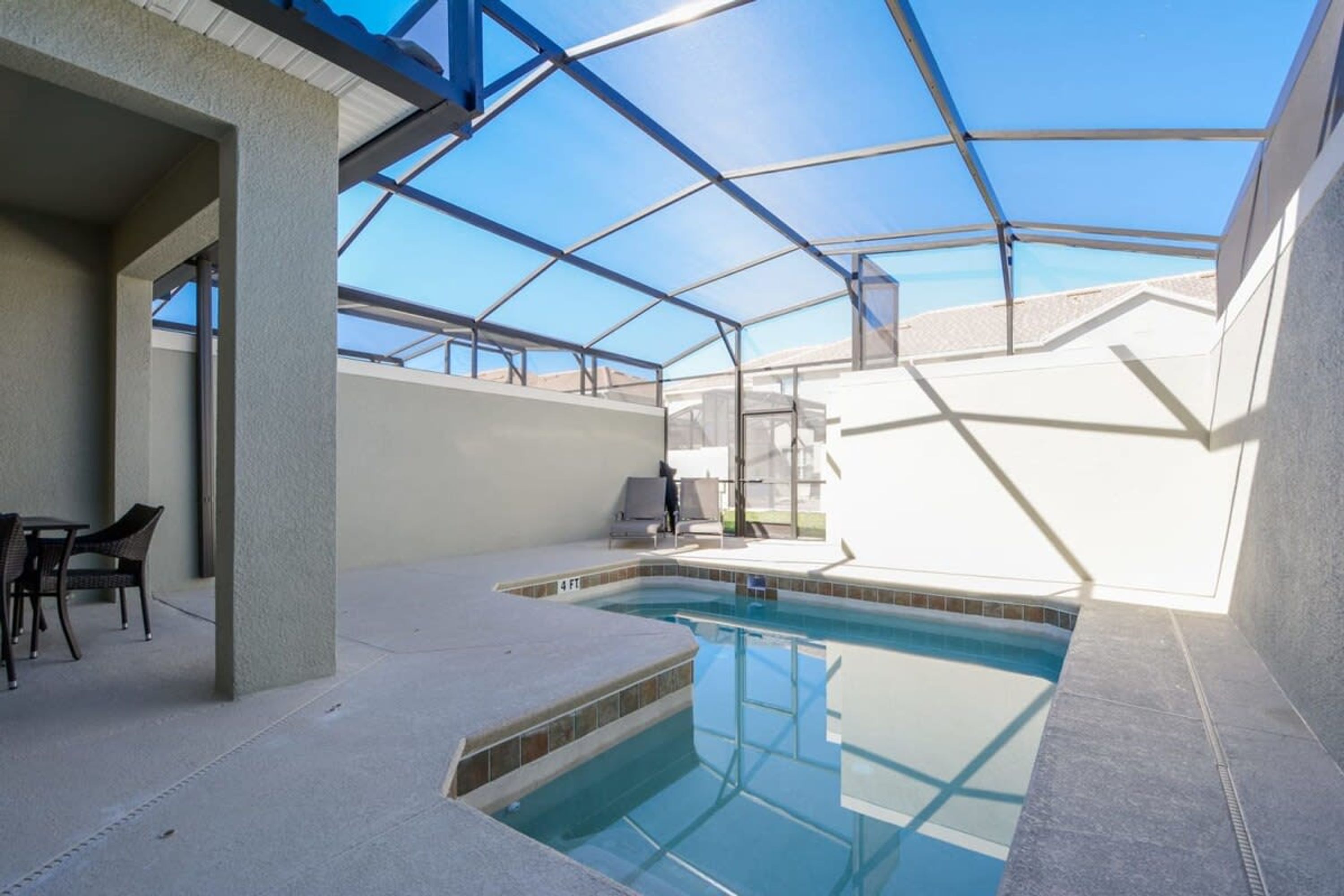 A swimming pool with a glass ceiling, surrounded by chairs and a table.