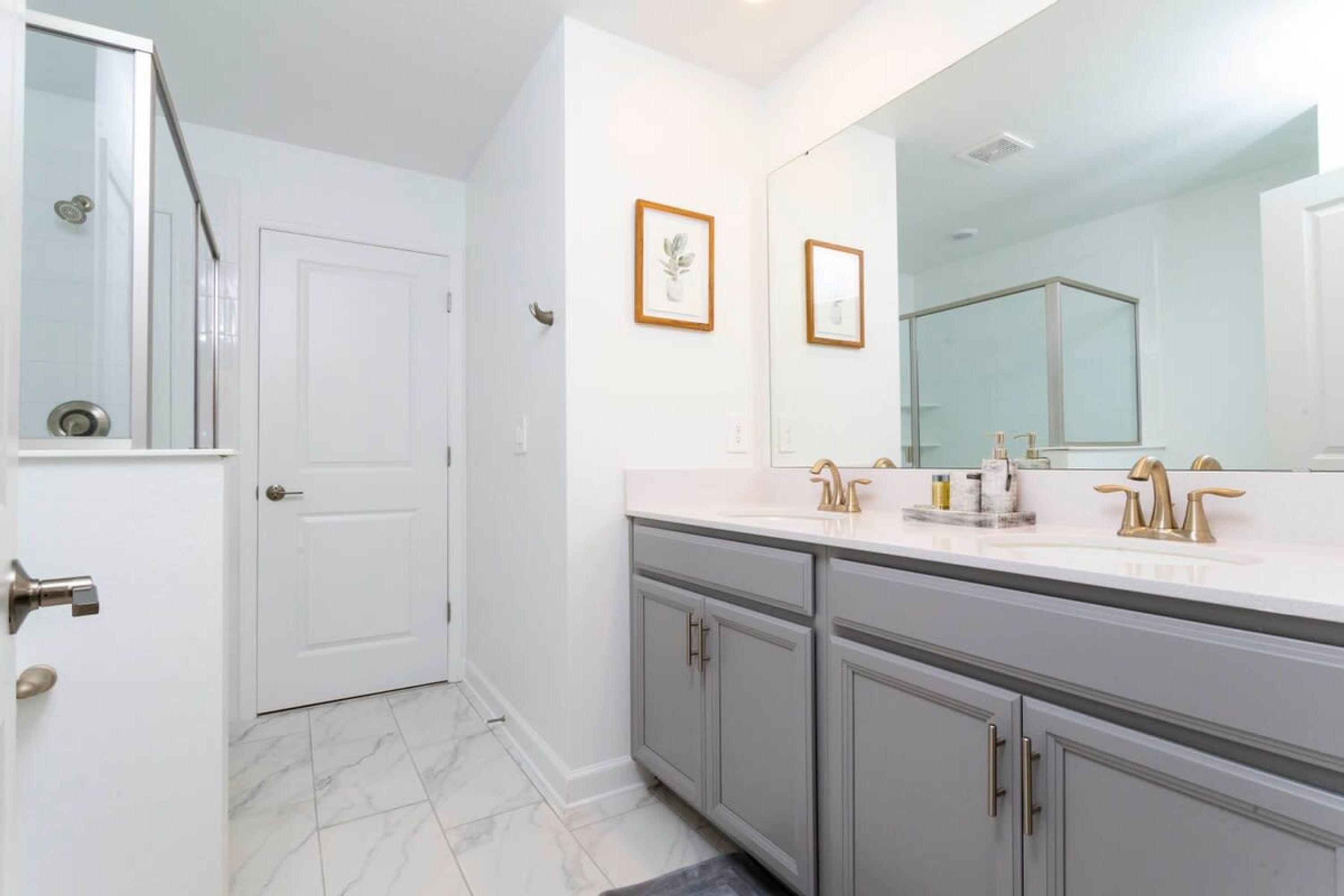 A bathroom with a double sink, a large mirror, and a door.
