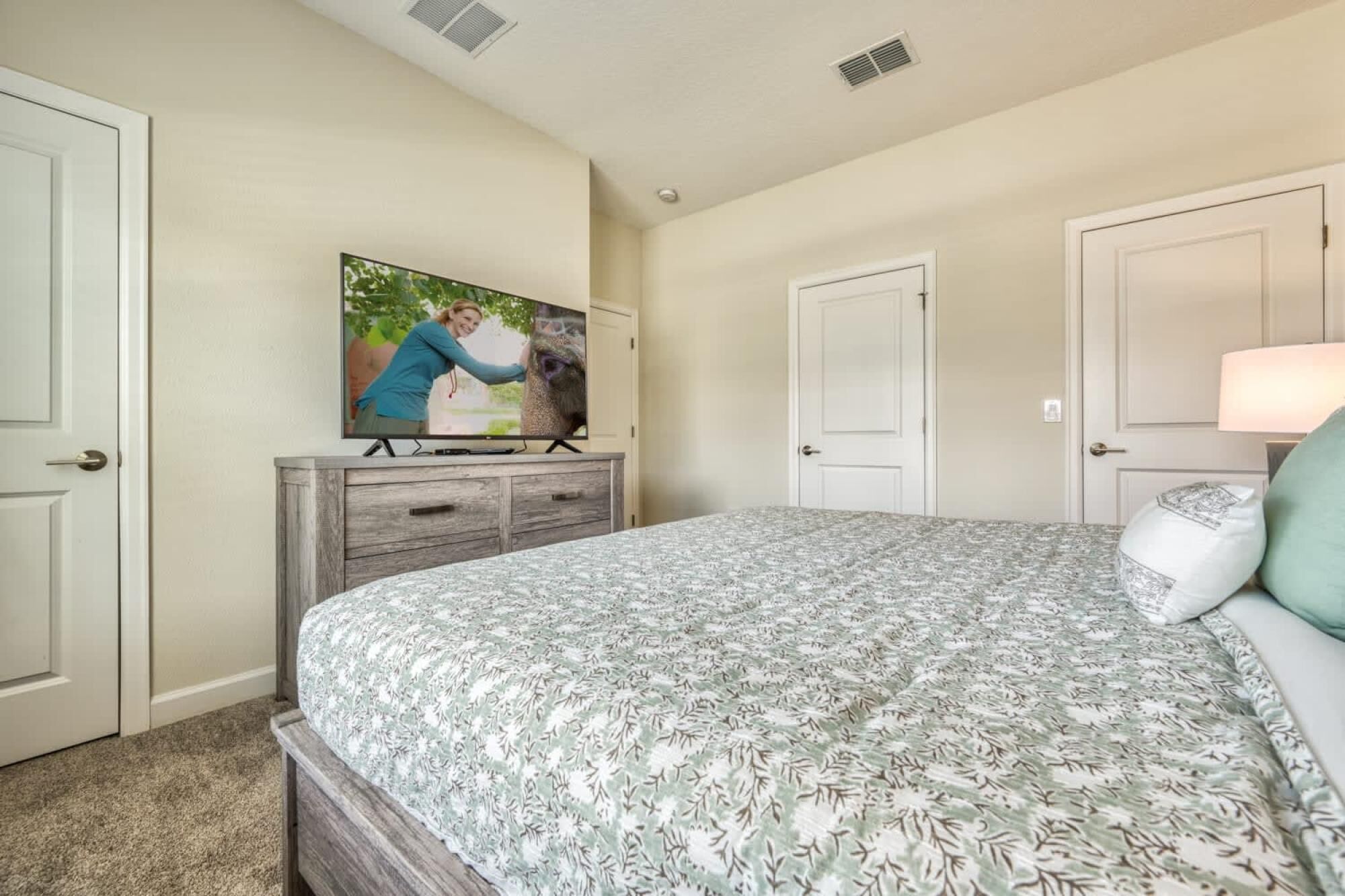 A bedroom with a bed, a dresser, a television on the wall, and two doors.