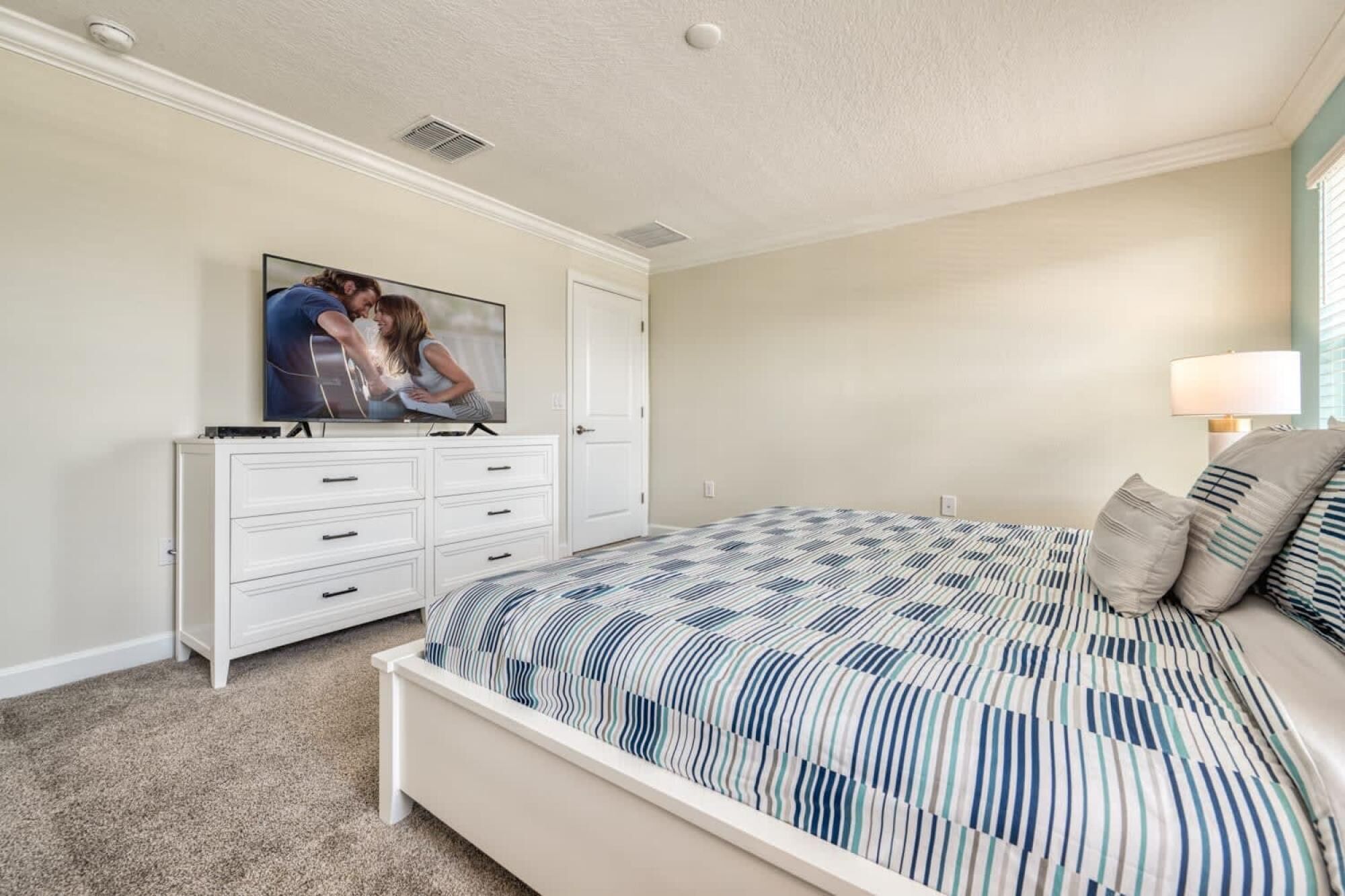 A bedroom with a bed, a dresser, a television, and a lamp.