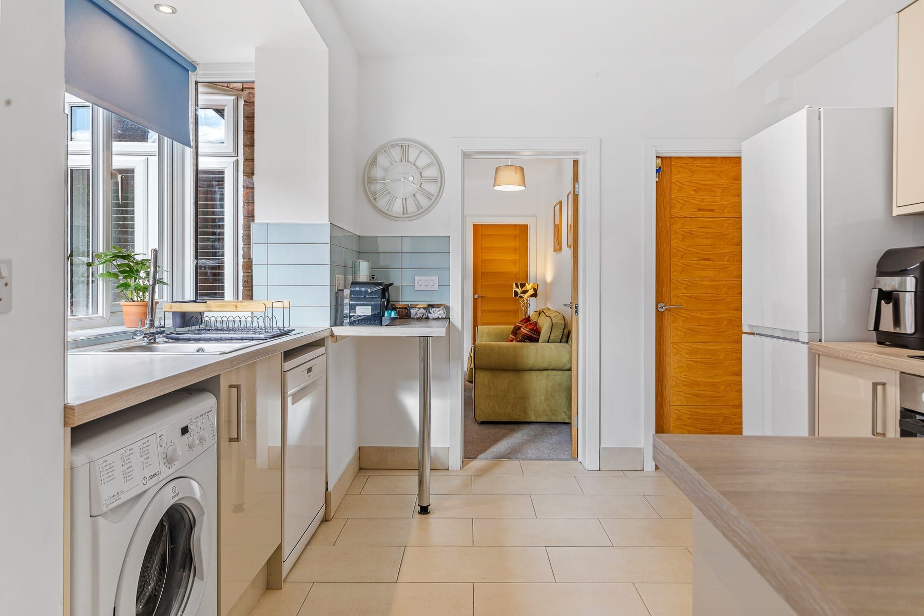 A compact kitchen with a washing machine, a coffee machine, and a dining area with a wooden door.